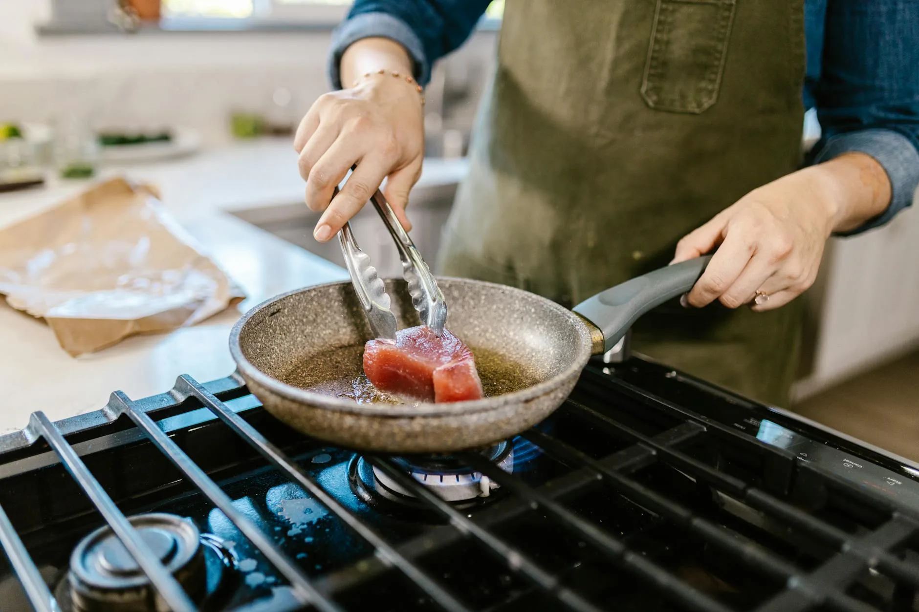 female hands holding frying pan and putting chunk of meat in hot frying oil