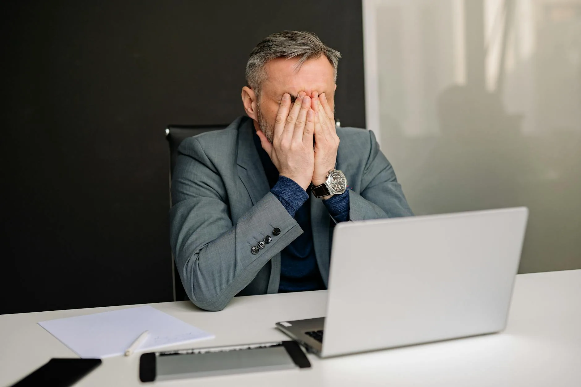 man in gray suit sitting on black chair covering his face
