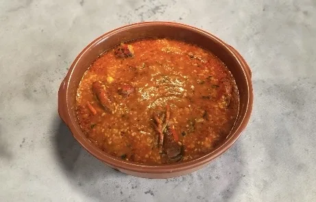Arroz con bogavante en cazuela de barro, trozos de bogavante y gambones, caldo sabroso con hierbas, inspirado en recetas de arroz mediterráneo